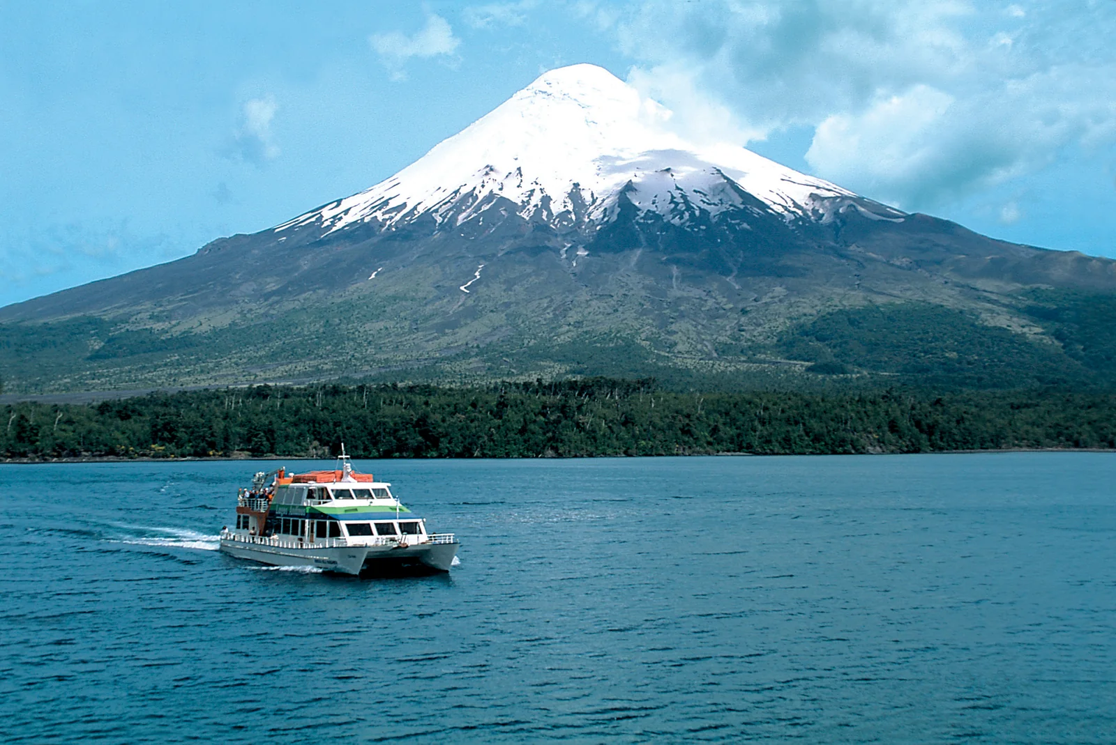 Boat crossing a lake beneath a snow-capped volcano on the Andean lake crossing